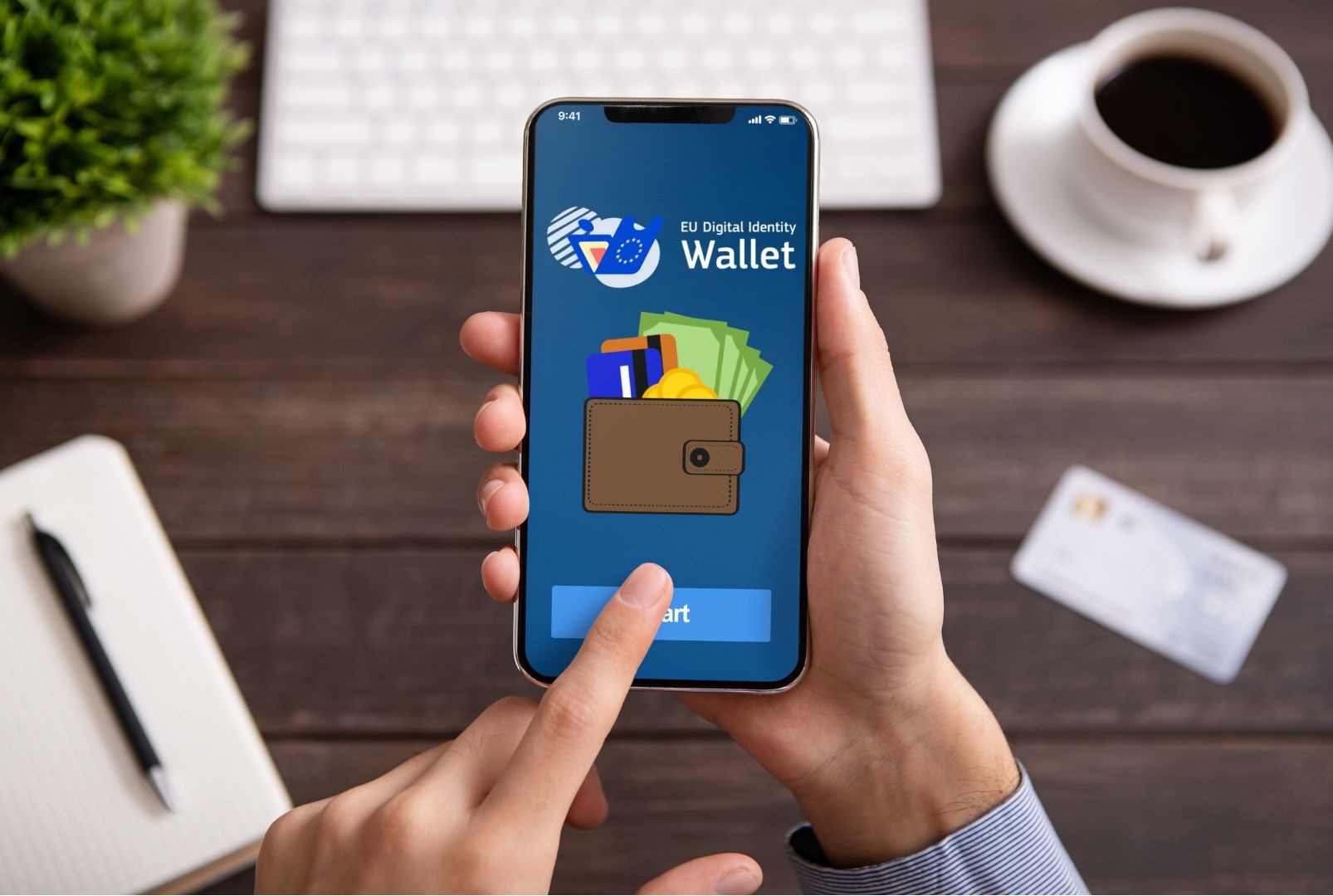 Mann tippt auf einem Smartphone, dort ist die EUDI-Wallet App zu sehen, im Hintergrund ist ein Schreibtisch mit einem Kaffee